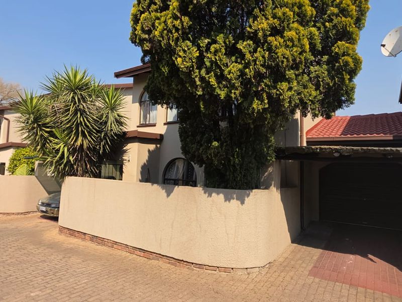 Front elevation of a townhouse complex featuring a paved driveway, boundary walls, and a covered carport area.