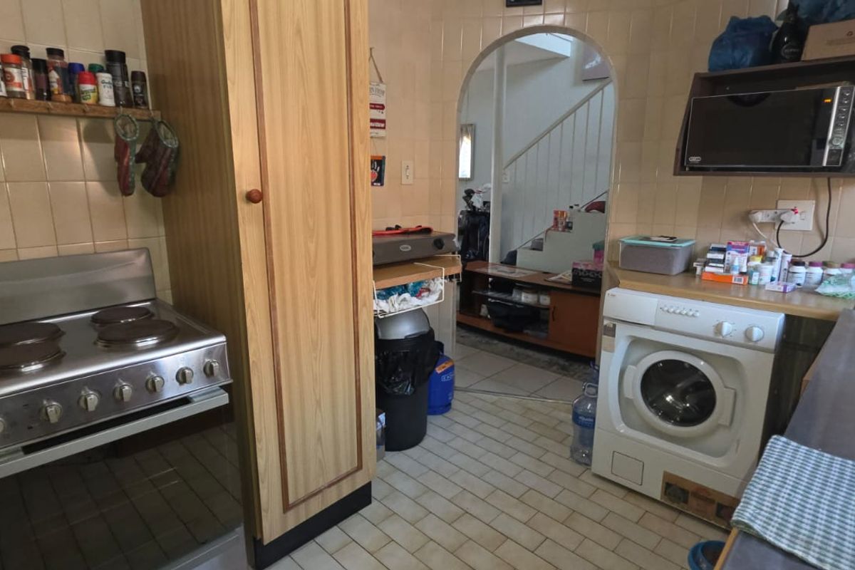 A functional kitchen featuring dated cabinetry, tiled splashbacks, a built-in electric stove, and a dedicated space for a washing machine.