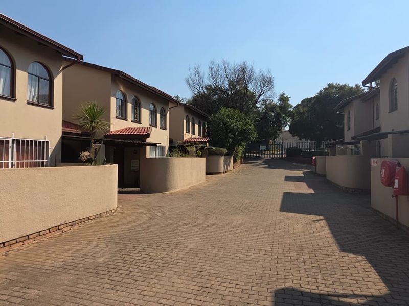 A view of the paved driveway and entrance area of the townhouse complex, featuring boundary walls and residential building facades.