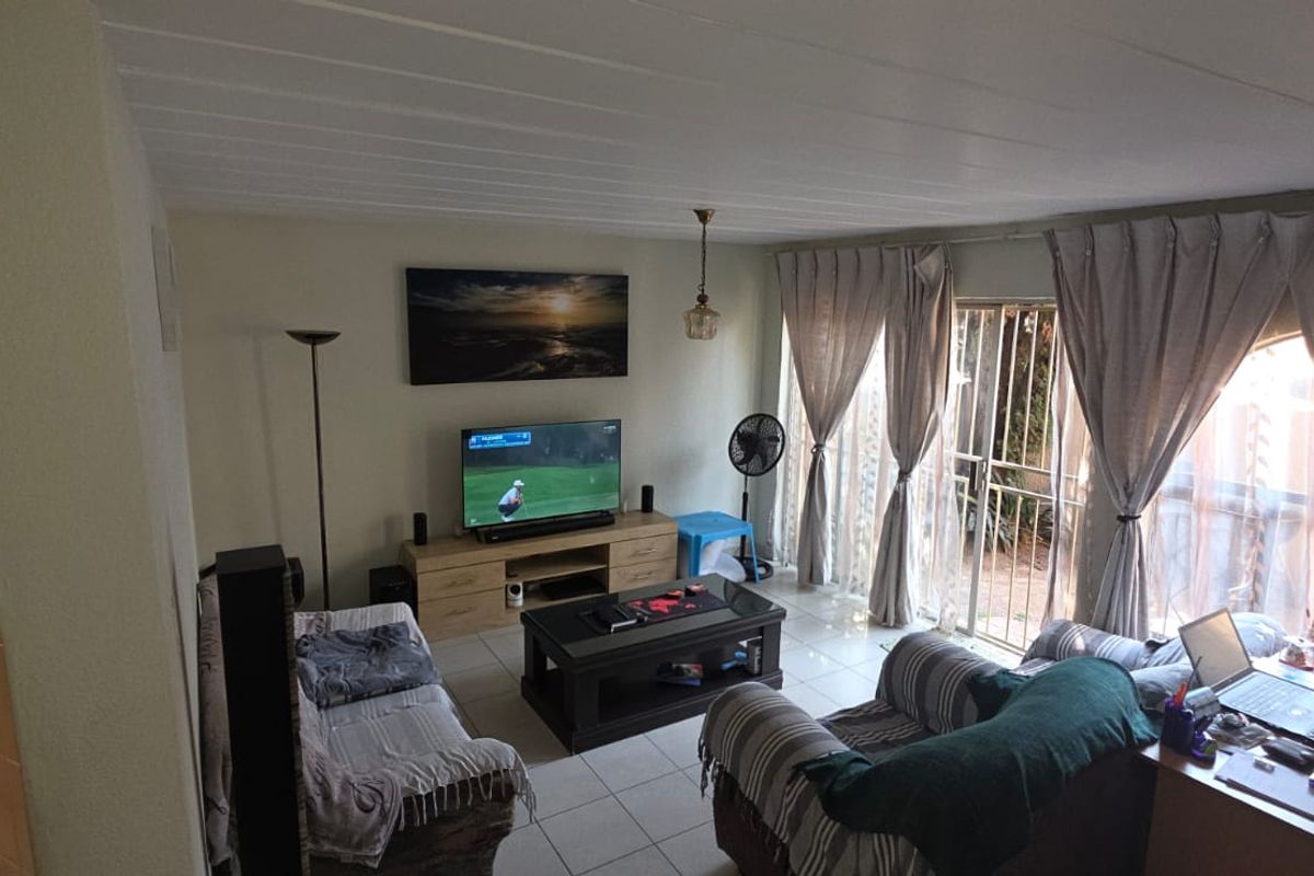 A living room featuring tiled flooring and a sliding glass door providing access to the exterior, with a view into the adjacent kitchen area.