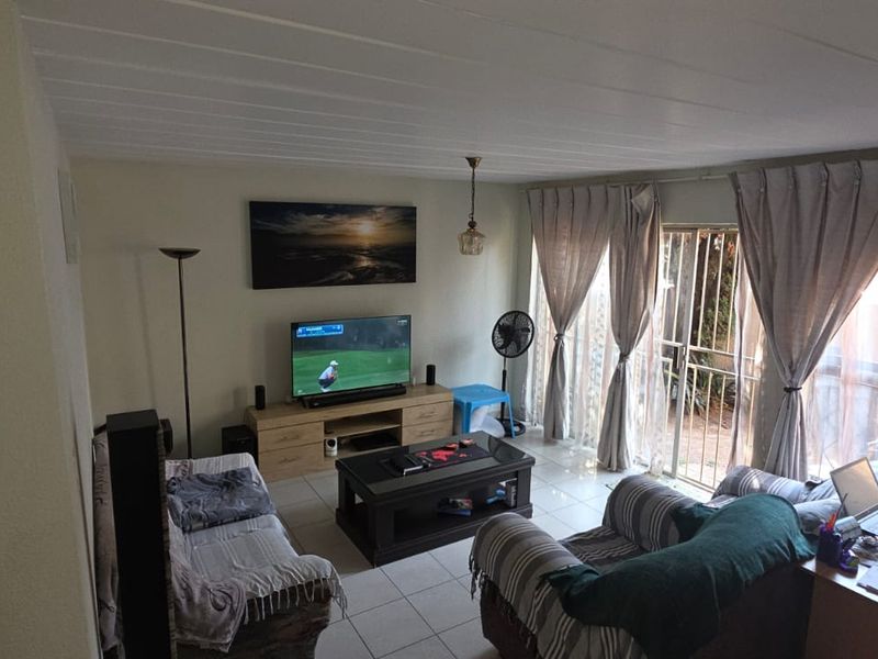 A living room featuring tiled flooring and a sliding glass door providing access to the exterior, with a view into the adjacent kitchen area.