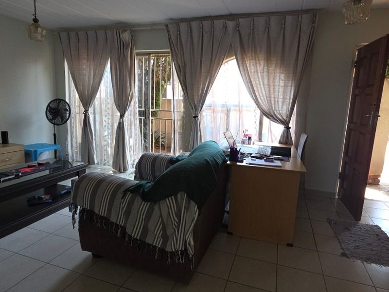 A living room featuring tiled flooring and a sliding glass door with security gate, providing access to the exterior.