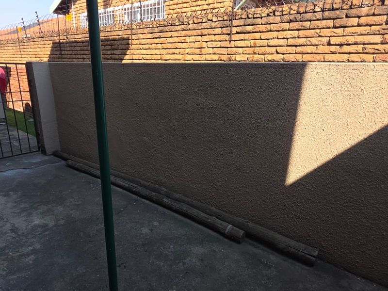 A rear exterior courtyard area featuring a perimeter brick wall with security spikes and a metal security gate.