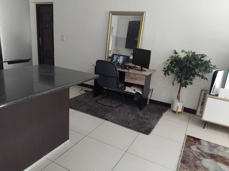 Open plan living area featuring tiled flooring and a granite kitchen countertop, currently utilized as a combined living and workspace.