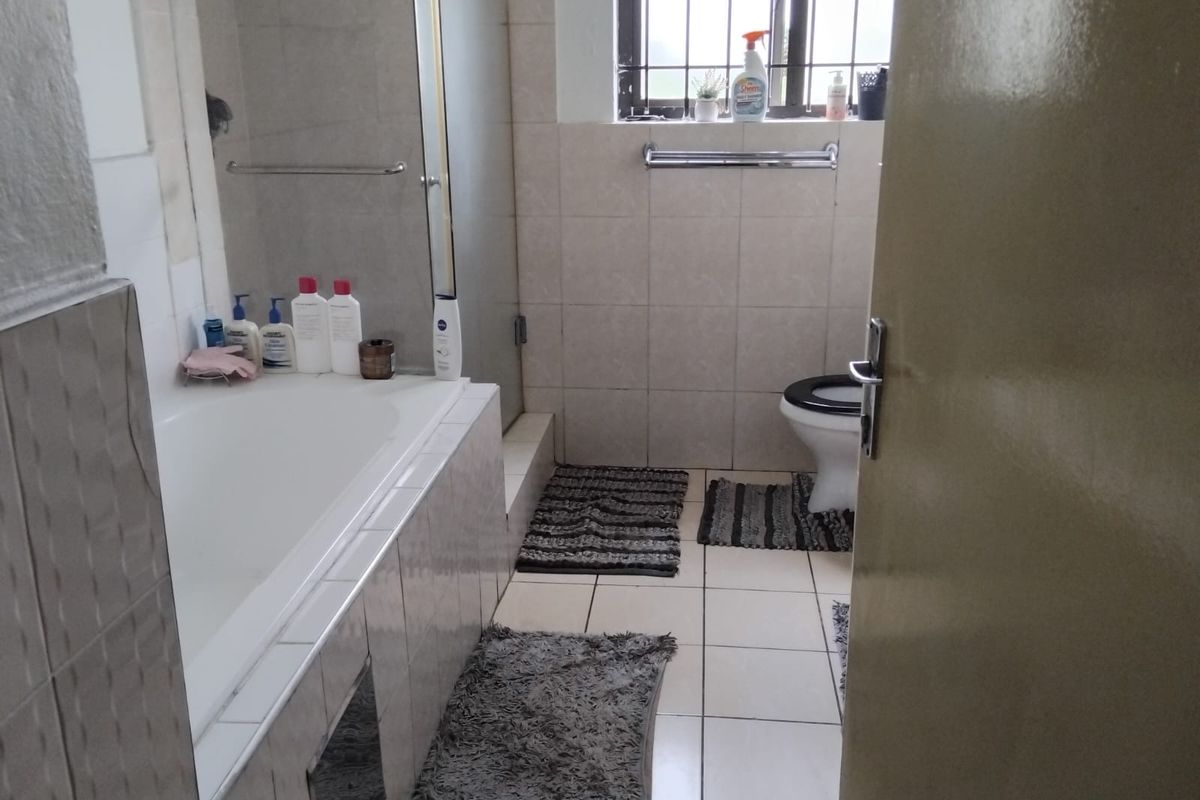 A functional bathroom featuring a bathtub, separate shower enclosure, and toilet, finished with neutral wall and floor tiling.