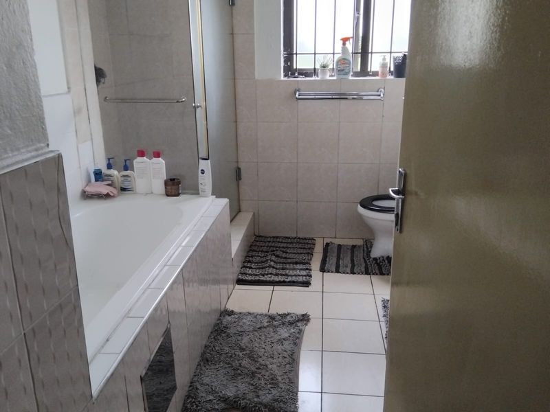 A functional bathroom featuring a bathtub, separate shower enclosure, and toilet, finished with neutral wall and floor tiling.