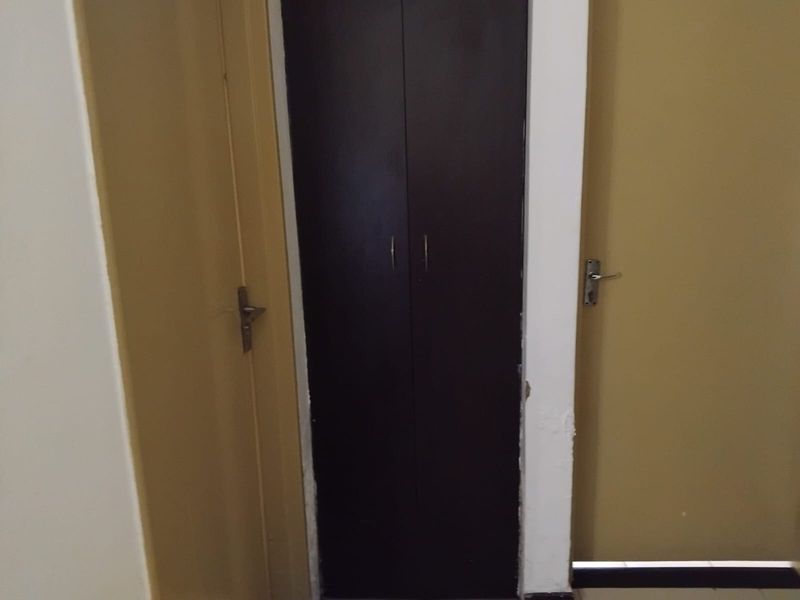A narrow hallway featuring a dark built-in cupboard flanked by two internal doors, showing signs of wear on the surrounding door frames.