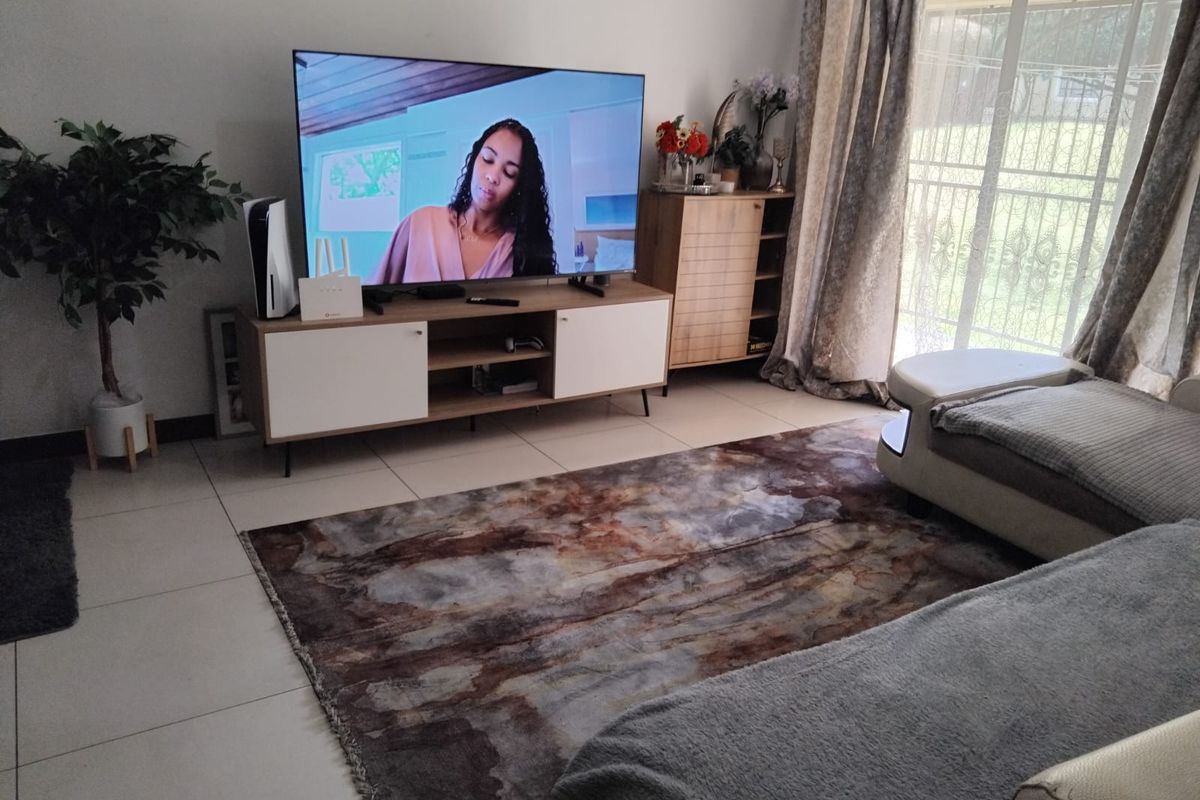 A comfortable living room featuring large format floor tiles and a sliding glass door with security gate providing access to the exterior.