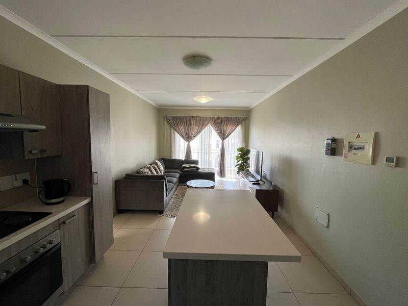 Open-plan living area featuring a modern kitchen with built-in cabinetry, stone countertops, and tiled flooring, flowing into a comfortable lounge space with balcony access.