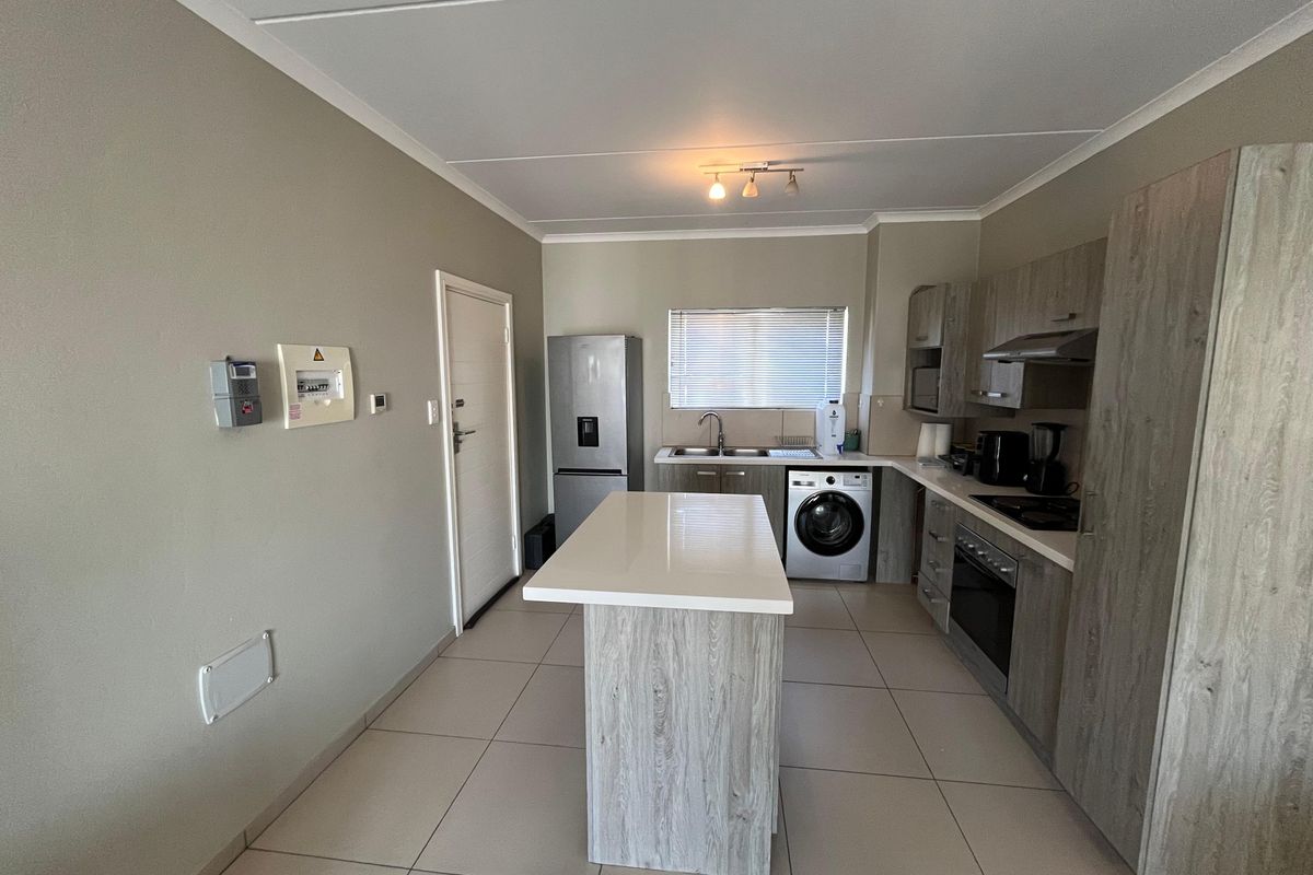 Modern kitchen featuring a central island, wood-look cabinetry, built-in oven and hob, and tiled flooring with integrated laundry appliance space.
