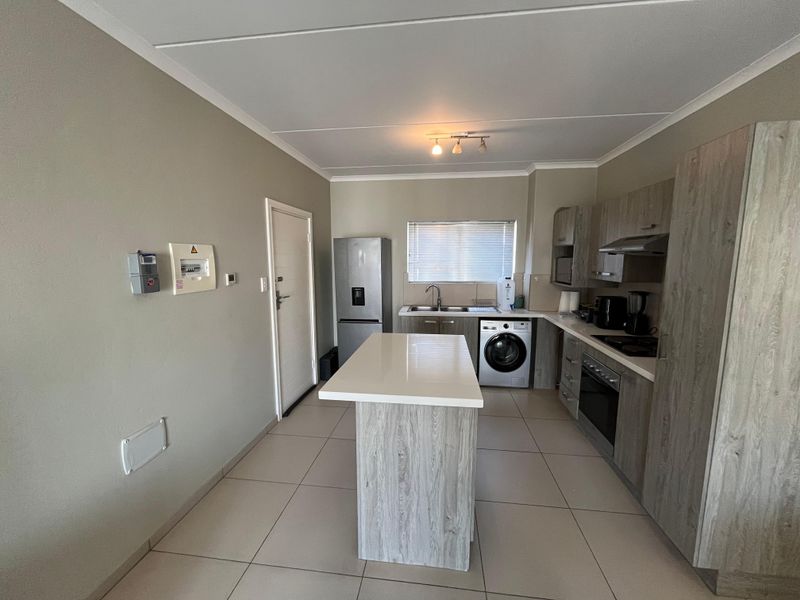 Modern kitchen featuring a central island, wood-look cabinetry, built-in oven and hob, and tiled flooring with integrated laundry appliance space.