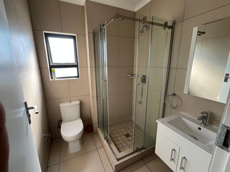 A clean, modern bathroom featuring a glass shower enclosure, a white vanity with a basin, and neutral floor-to-ceiling wall tiles.