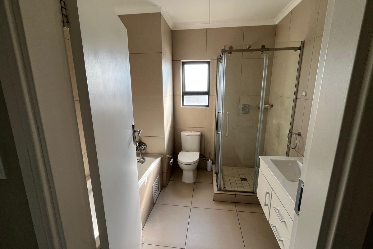 A clean, modern bathroom featuring a glass-enclosed shower, a built-in bathtub, and a vanity cabinet with neutral wall and floor tiling.