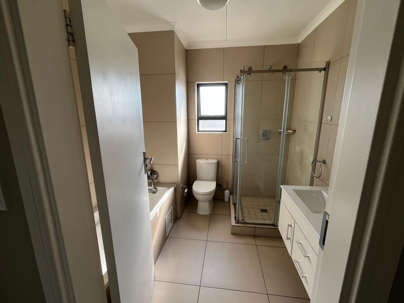 A clean, modern bathroom featuring a glass-enclosed shower, a built-in bathtub, and a vanity cabinet with neutral wall and floor tiling.