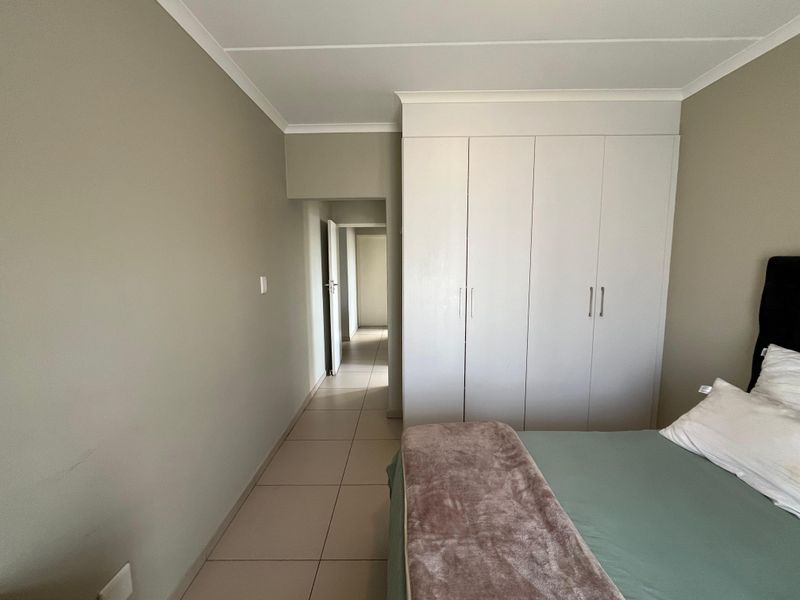 A well-maintained bedroom featuring neutral wall tones, built-in cupboards, and tiled flooring, leading into a hallway.