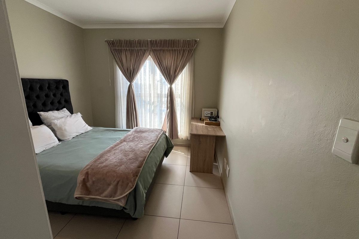 A well-maintained bedroom featuring neutral wall tones, tiled flooring, and a window with installed curtain tracks.
