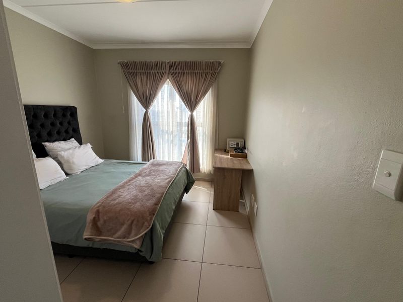 A well-maintained bedroom featuring neutral wall tones, tiled flooring, and a window with installed curtain tracks.