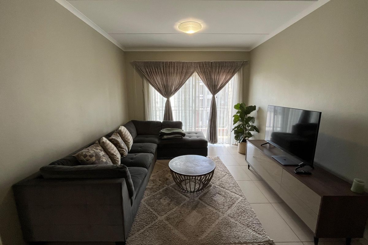 A comfortable living room featuring neutral wall tones, tiled flooring, and a sliding glass door providing access to the balcony.