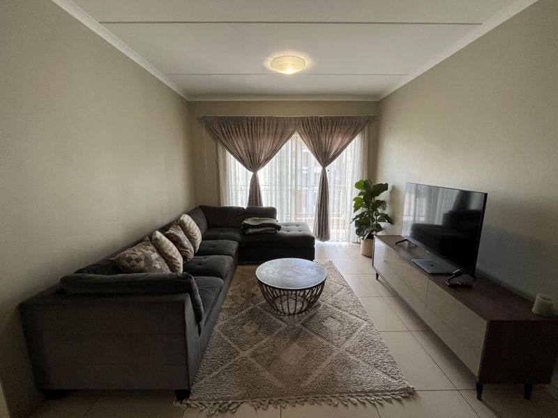 A comfortable living room featuring neutral wall tones, tiled flooring, and a sliding glass door providing access to the balcony.