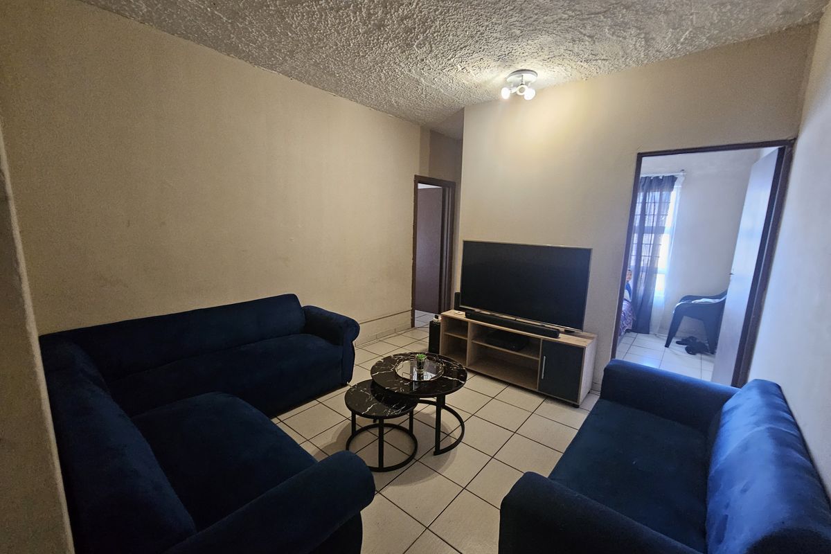 A living room featuring tiled flooring and a textured ceiling, providing a functional space with potential for cosmetic updates.