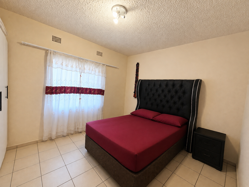A bedroom featuring tiled flooring, a textured ceiling, and a built-in wardrobe, providing a functional and neutral living space.