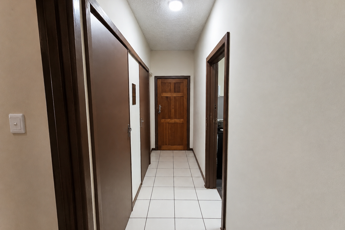 A clean and functional hallway featuring tiled flooring, built-in storage cupboards, and a solid wood door leading to another room.