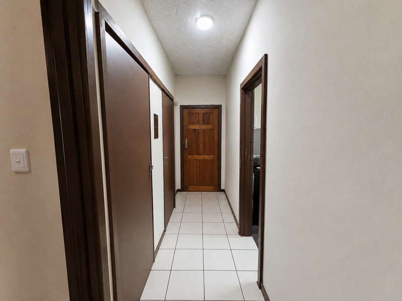 A clean and functional hallway featuring tiled flooring, built-in storage cupboards, and a solid wood door leading to another room.