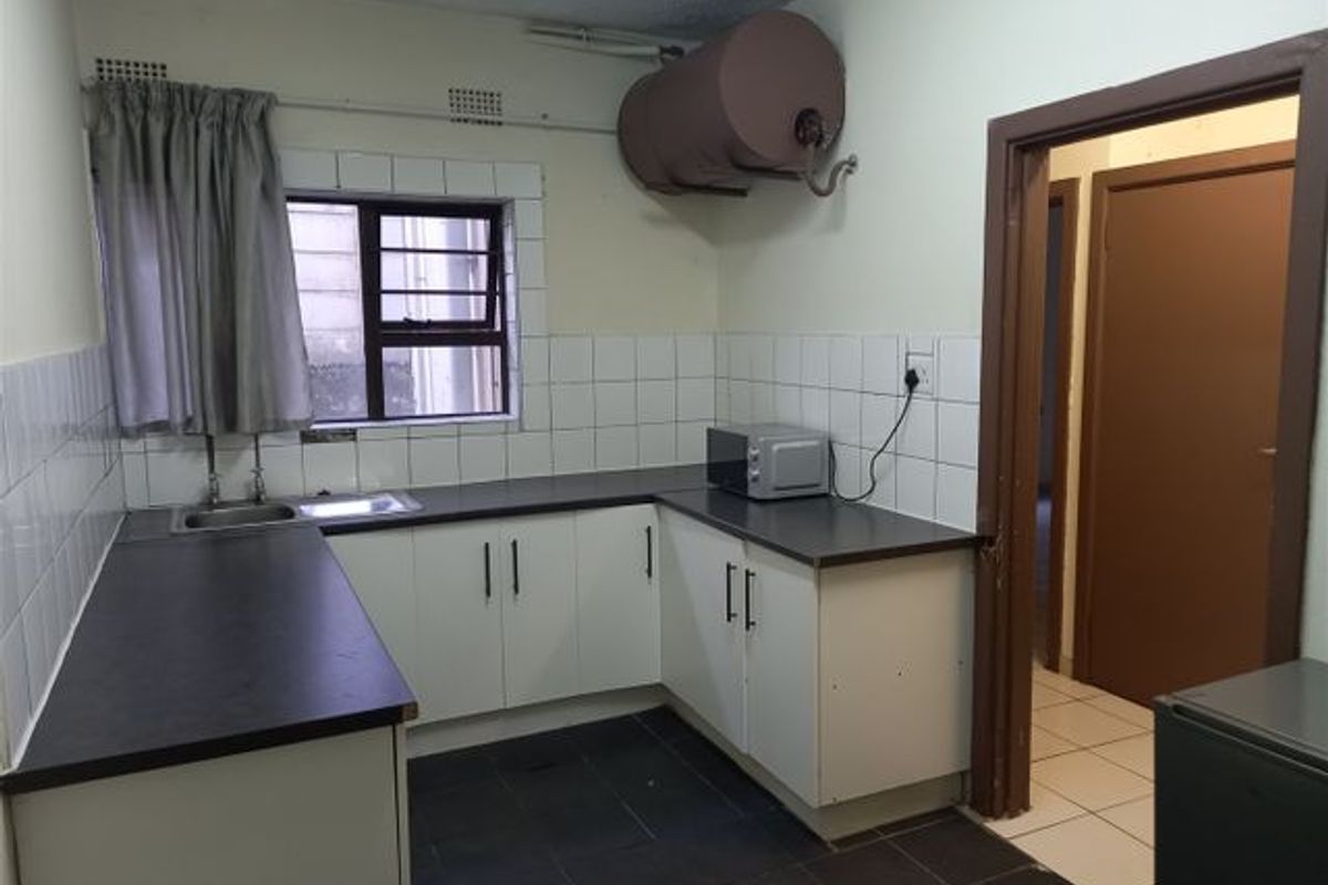 A functional kitchen featuring built-in cabinetry, laminate countertops, tiled splashbacks, and an electric water heater, offering a blank canvas for renovation.