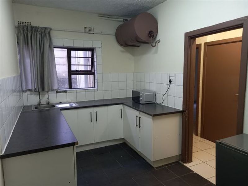 A functional kitchen featuring built-in cabinetry, laminate countertops, tiled splashbacks, and an electric water heater, offering a blank canvas for renovation.