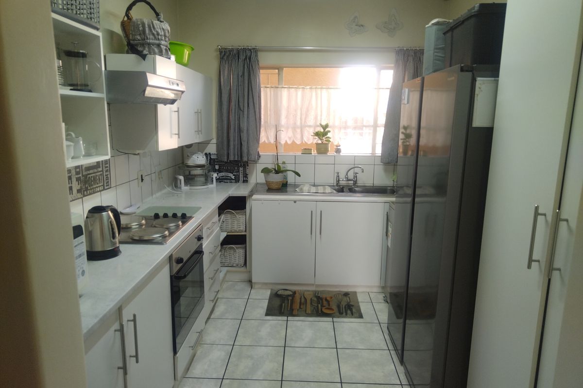 A functional galley-style kitchen featuring white cabinetry, tiled flooring, a built-in oven, and an electric hob with an extractor fan.