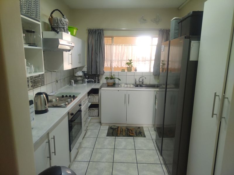 A functional galley-style kitchen featuring white cabinetry, tiled flooring, a built-in oven, and an electric hob with an extractor fan.