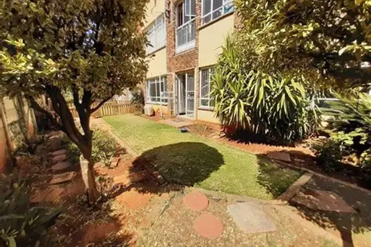 A rear view of the apartment building featuring a private garden area with a lawn, paved stepping stones, and direct access via a sliding door.