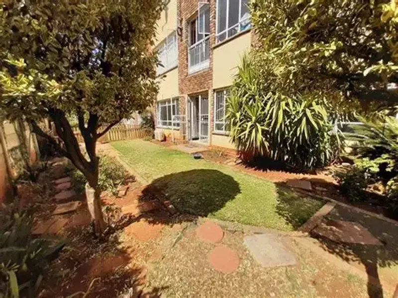A rear view of the apartment building featuring a private garden area with a lawn, paved stepping stones, and direct access via a sliding door.