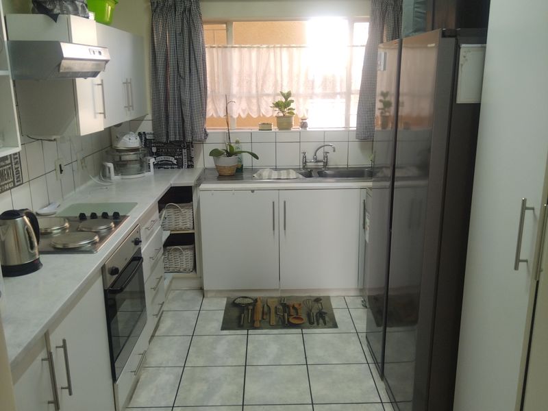 A functional galley-style kitchen featuring white cabinetry, tiled flooring, a built-in oven, hob, and a stainless steel sink with a window view.