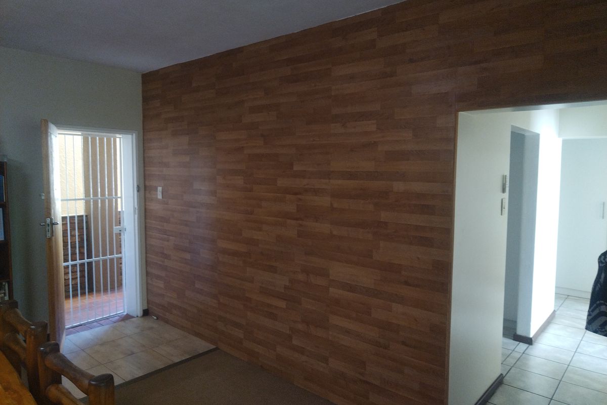 Living area featuring wood-look wall paneling, tiled and carpeted flooring, and a security gate leading to an outdoor space.
