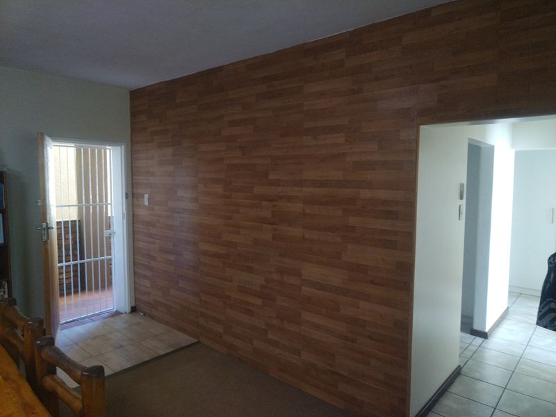 Living area featuring wood-look wall paneling, tiled and carpeted flooring, and a security gate leading to an outdoor space.