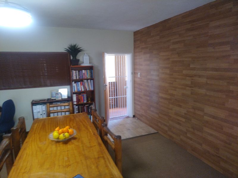 Dining area featuring wood-look wall paneling, a ceiling light fixture, and a security gate leading to an outdoor space.