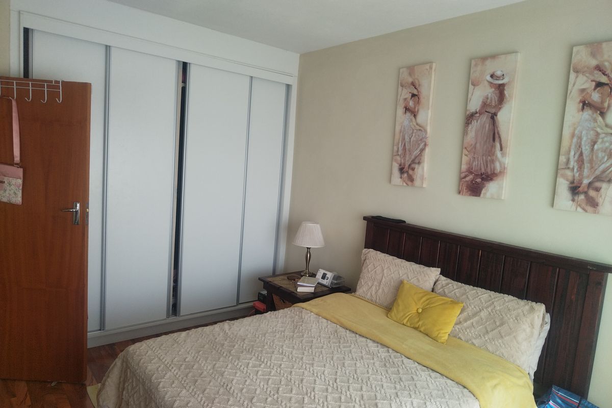 A functional bedroom featuring timber flooring and a large built-in sliding door wardrobe with white finish.