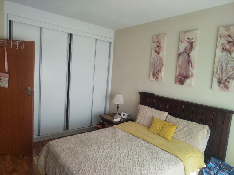 A functional bedroom featuring timber flooring and a large built-in sliding door wardrobe with white finish.