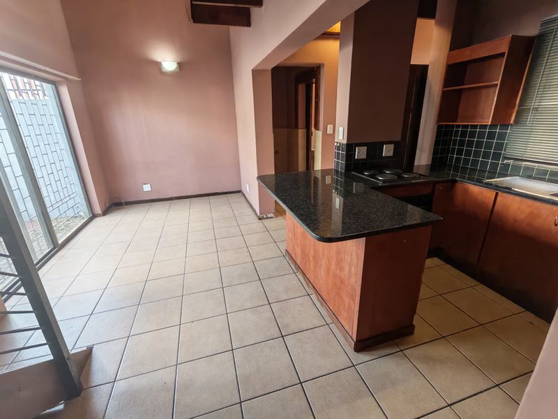 Open-plan kitchen and living area featuring granite countertops, wooden cabinetry, ceramic tile flooring, and direct access to an outdoor space via a sliding door.