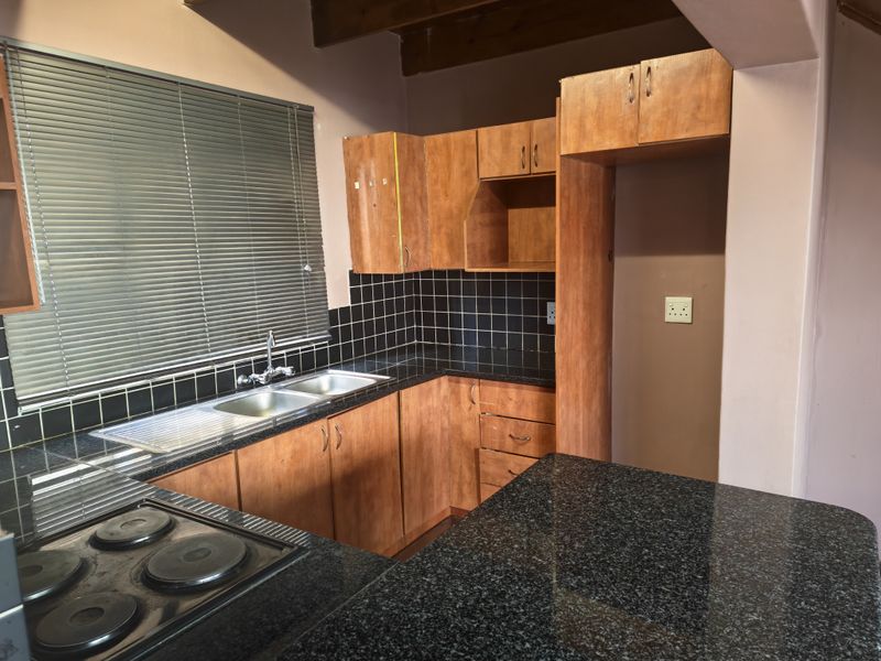 A functional kitchen featuring wooden cabinetry, granite countertops, a double basin sink, and a built-in electric hob with exposed timber ceiling beams.