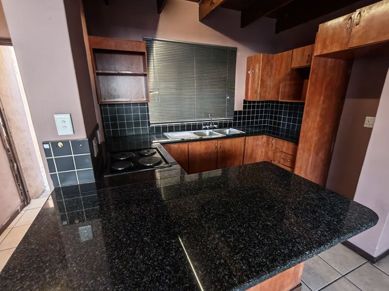 A functional kitchen featuring dark granite countertops, wooden cabinetry, a built-in electric hob, and a double basin sink with a tiled backsplash.