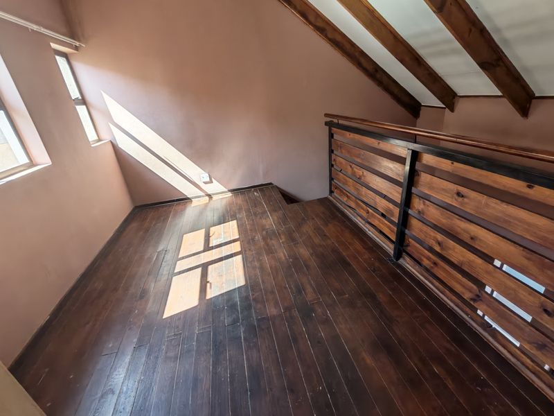 An open mezzanine landing area featuring polished timber flooring, exposed wooden rafters, and a sturdy timber and metal balustrade.