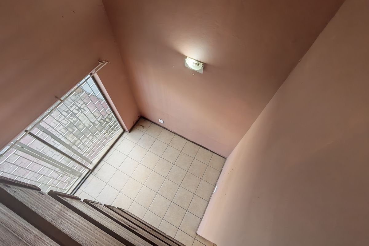 An empty, tiled living area featuring a security gate and wall-mounted lighting, offering a blank canvas for potential interior design updates.