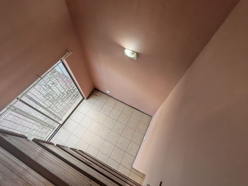 An empty, tiled living area featuring a security gate and wall-mounted lighting, offering a blank canvas for potential interior design updates.