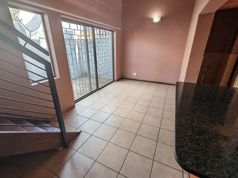 An open-plan living area featuring tiled floors, a granite breakfast bar, and a sliding door leading to an outdoor space with security gates.