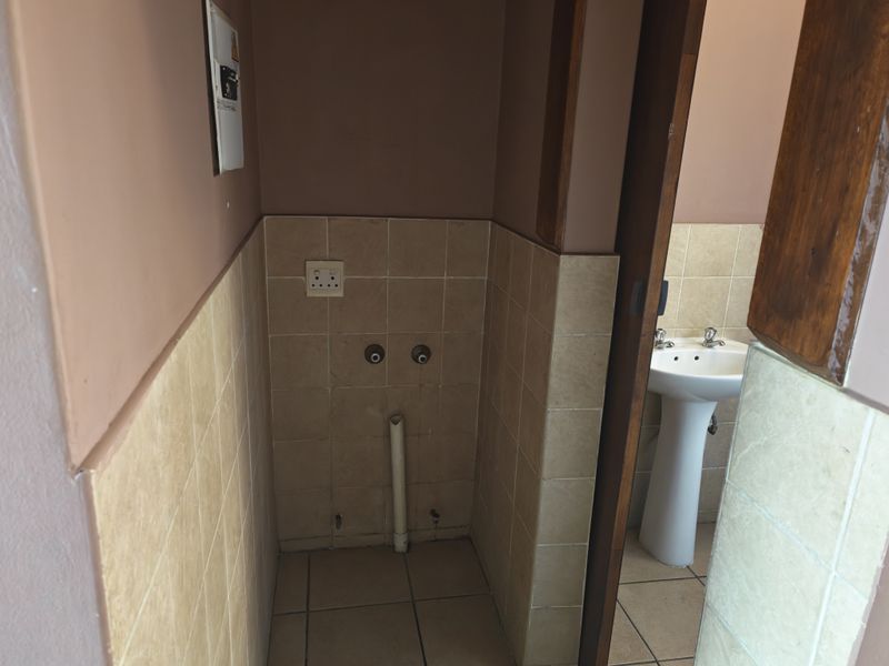 A functional laundry area featuring tiled finishes, dedicated plumbing connections for appliances, and an adjacent pedestal basin.