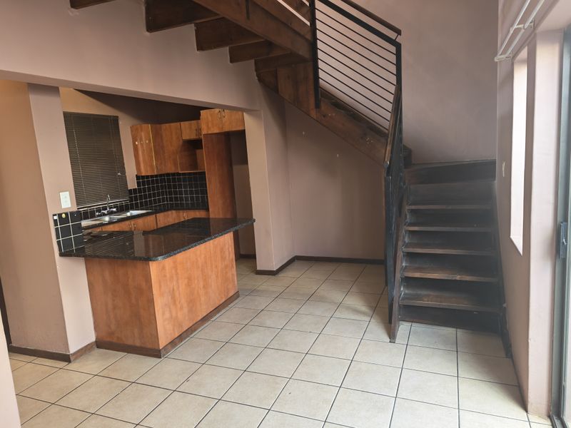 Open plan living area featuring a wooden staircase, tiled flooring, and a functional kitchen with granite countertops and built-in cabinetry.