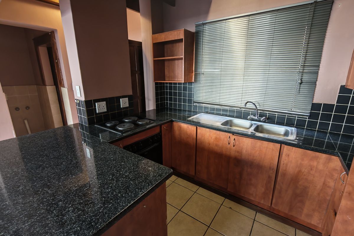 A functional kitchen featuring granite countertops, wooden cabinetry, built-in oven, electric hob, and a double bowl sink with tiled backsplash.