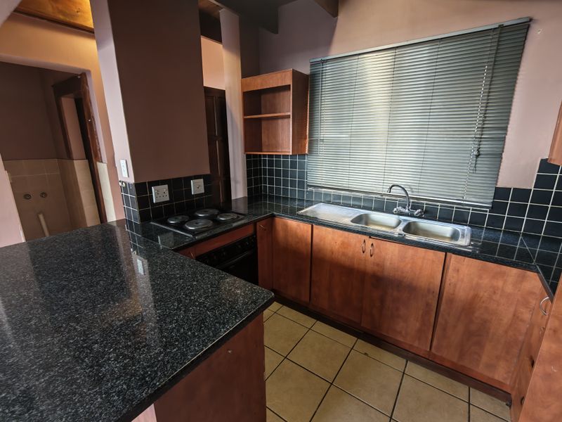 A functional kitchen featuring granite countertops, wooden cabinetry, built-in oven, electric hob, and a double bowl sink with tiled backsplash.